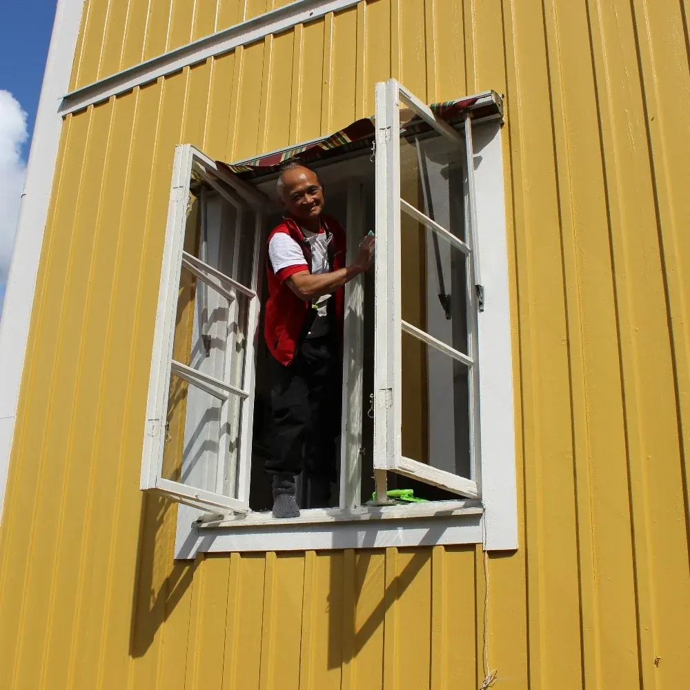 Medarbetare från Linde-Handtaget putsar ett fönster på ett gult trähus